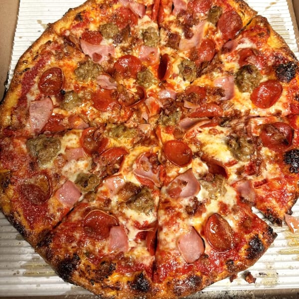 A whole MT's Pizza King pizza with pepperoni, ham, and sausage toppings in a box.