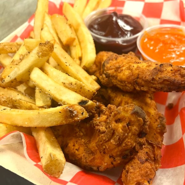 Crispy chicken tenders and seasoned french fries in a red and white checkered basket with dipping sauces.
